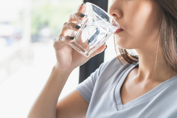 Close up view of young woman drinking pure mineral water in a glass.