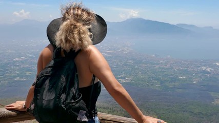 Rear back shot of a woman standing on a high viewpoint overlooking the city and the sea