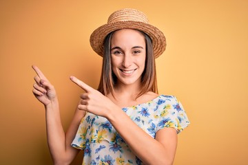 Young beautiful woman wearing casual t-shirt and summer hat over isolated yellow background smiling and looking at the camera pointing with two hands and fingers to the side.