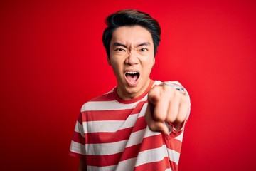 Young handsome chinese man wearing casual striped t-shirt standing over red background pointing...