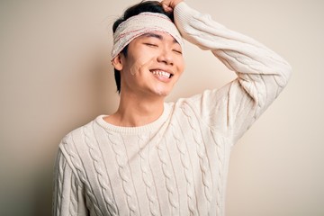 Young handsome chinese man injured for accident wearing bandage and strips on head smiling confident touching hair with hand up gesture, posing attractive and fashionable