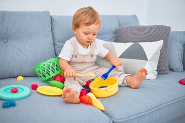 Adorable blonde toddler sitting on the sofa playing with plastic meals toys at home