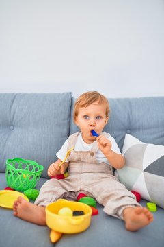 Adorable blonde toddler sitting on the sofa playing with plastic meals toys at home