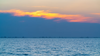 Colorful sunrise at sea, oil platforms in distance