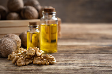 Glass bottle with walnut oil and walnut kernel on a wooden table. Cosmetic and therapeutic product. Selective focus.