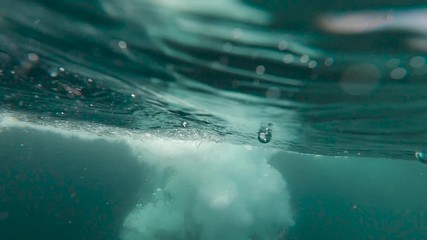Slow motion 240 FPS underwater shot of water splashes in the sea after a man jumps from cliffs inside the sea