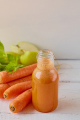 Healthy eating, dieting and vegetarian concept - glass jugs of carrot, apple  and celery juice with vegetables on light wooden background 