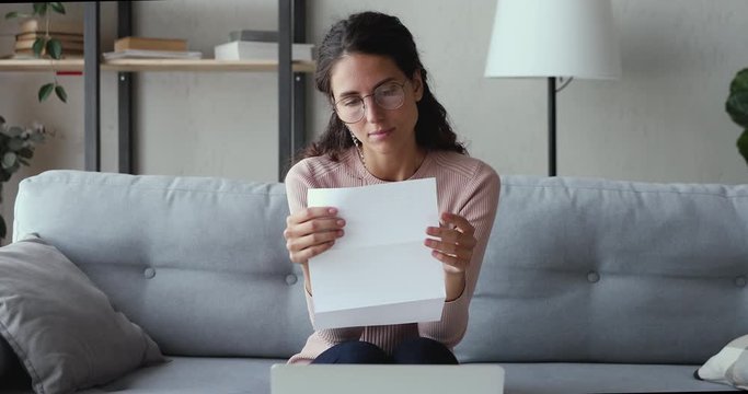 Stressed worried young woman reading bad news in paper mail letter at home. Desperate lady frustrated about bankruptcy, financial problem, receiving bank debt penalty, high bills, lost job concept.