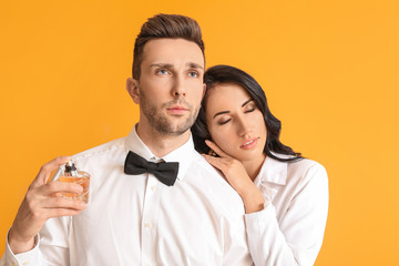 Stylish young couple with perfume on color background