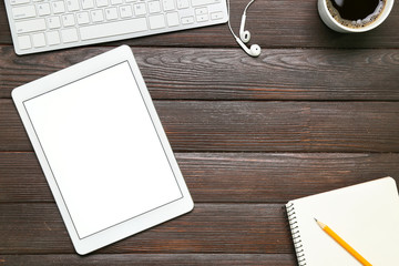 Tablet computer, PC keyboard and stationery on wooden background