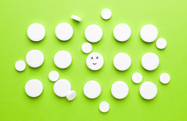 One pill with drawn happy face among white ones on color background