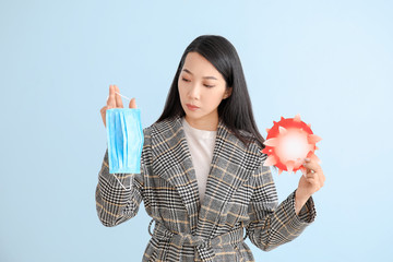 Asian woman with protective mask and model of Coronavirus on color background. Concept of epidemic