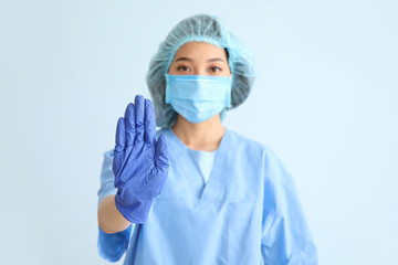 Asian doctor showing stop gesture on color background. Concept of epidemic