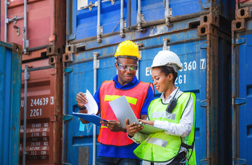 Happy worker man in hardhat and safety vest holding clipboard checklist and Female foreman using laptop control loading containers box from cargo