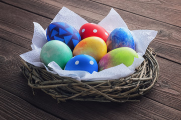 Colored painted easter eggs in a nest of twigs with white napkins on a wooden rustic background.