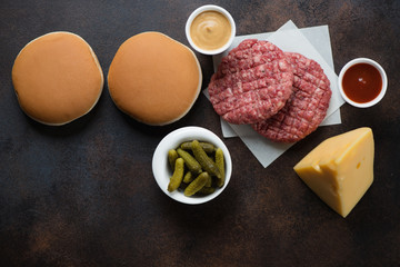 Raw beef cutlets and burger buns over dark brown metal background, horizontal shot with copy space, above view