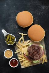 Double burger with marbled beef cutlets, fries, pickles and buns. Flatlay on a dark metal background, vertical shot