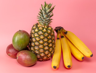 Pineapple, bananas and mangoes on a pink background