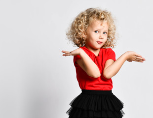 Curly hair blonde kid girl in red t-shirt holds hands up with open palms