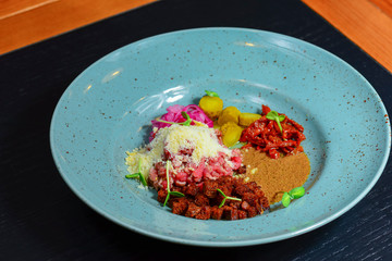 Vegetable salad with sause served on a blue plate on dark rustic wooden table in restaurant.