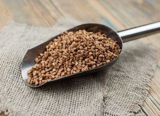 Raw, natural, uncooked buckwheat seed kernels in metal scoop on wooden table