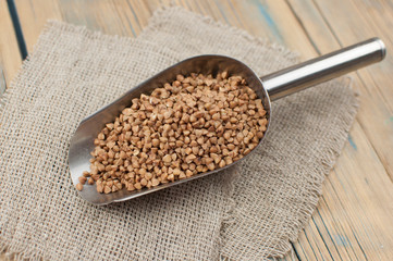 Raw, natural, uncooked buckwheat seed kernels in metal scoop on wooden table