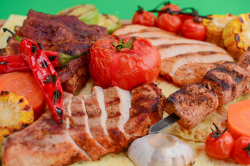 Top view of grilled meal of steak and vegetables spread out on rustic wooden board over bright green background