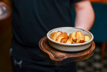 Waiter serves baked potatoes in a restaurant. Delicious food, baked potatoes with spices on white plate