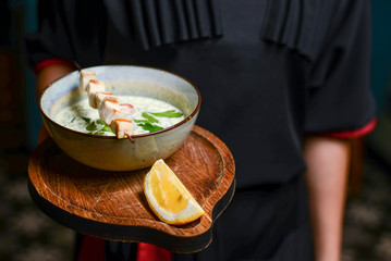 Waiter serves Okroshka in a restaurant. Summer light cold yogurt soup with cucumber, radish, eggs and dill on a board