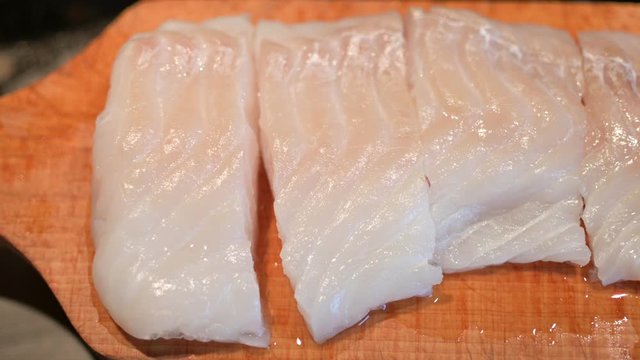 Close up shot of a cod fillet placed on a wooden cutting board and cut into portions.