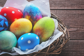 Closeup of colorful painted easter eggs on white napkins in a nest of twigs on an old wooden rustic table with copy space