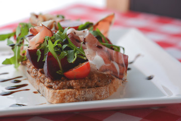 Italian appetizer bruschetta with roasted tomatoes, mozzarella cheese, garlic, herbs, prosciutto crudo and sauce.