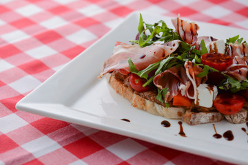 Italian appetizer bruschetta with roasted tomatoes, mozzarella cheese, garlic, herbs, prosciutto crudo and sauce.