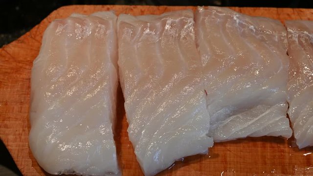 Close up shot of a cod fillet placed on a wooden cutting board and cut into portions.