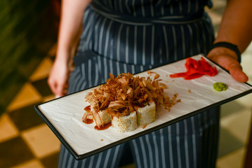 Waiter in a uniform holds a plate with sushi rolls in a restaurant. Food photography concept. Japanese cuisine.