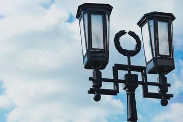 Fototapeta na wymiar Glowing burning lantern on an iron column and blue sky background close-up