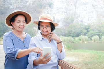 A senior Asian woman holds a smartphone, takes photos and plays social media. She enjoys retirement. Elderly community concept. Copy space