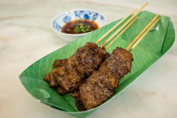 Grilled beef skewers  in a green paper dish. The side has a cup of sauce. Is a Chinese and Japanese style food.