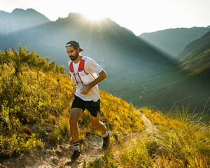 A trail runner at sunrise, running up a mountain trail above a valley in the mountains - 334371113