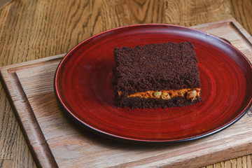 Homemade carrot cake with pumpkin, a piece of brownie cake served on red plate over dark rustic wooden background.