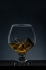 Elegant Glass with Cognac and Ice Cubes on Wooden Table. Copy Space Background