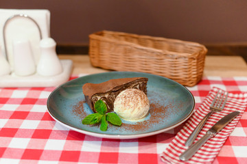 A piece of chocolate brownie pancake cake with vanilla ice-cream and chocolate sauce served on a blue plate.