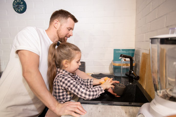 Cute little girl washing her mug over sink with duster and dish washer