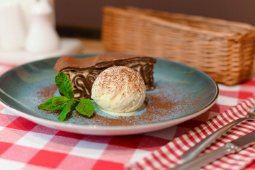 A piece of chocolate brownie pancake cake with vanilla ice-cream and chocolate sauce served on a blue plate.
