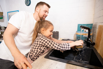 Fototapeta premium Happy young affectionate father helping his little daughter to wash her mug