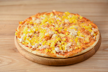 Fresh pizza with chicken meat, cheese and corn on wooden board over rustic wooden table background closeup.