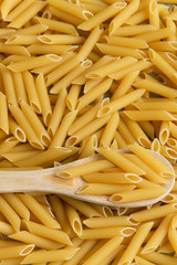 Food background -  dry penne pasta and wooden spoon, whole wheat uncooked ingredient