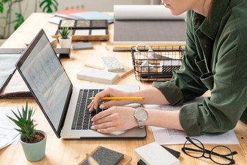 Young creative female designer bending over desk in front of laptop