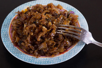 Close up caramelized onion on plate with fork on the black background