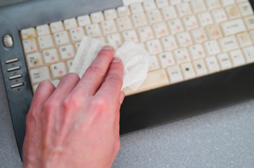 Person sanitizes a computer keyboard with antibacterial wipes. Close-up. Coronavirus Precautions concept